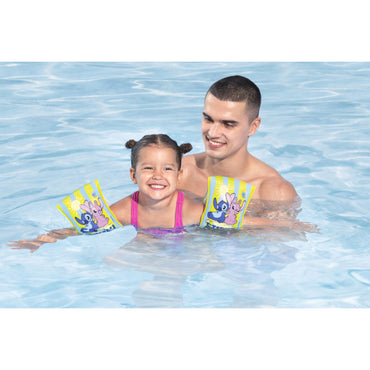 Niña sonriendo en la piscina con flotadores Disney Bestway 23x15cm, acompañada de un adulto.