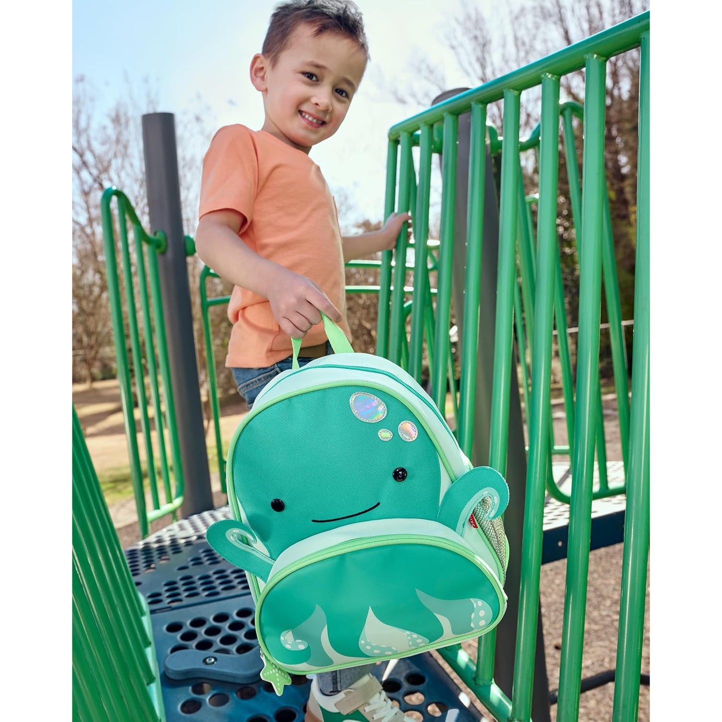 mochila infantil verde con diseño de pulpo, niño jugando en un parque