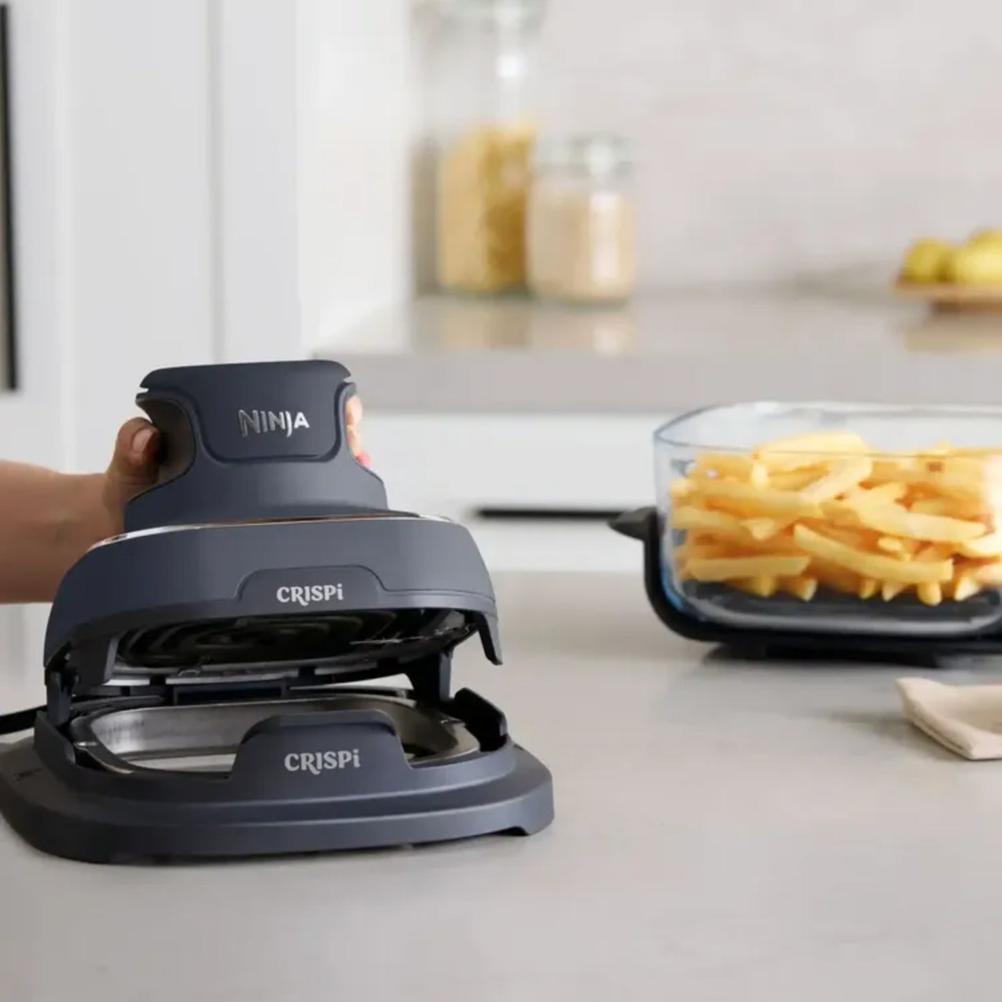 freidora de aire Ninja negra en cocina moderna, con papas fritas al fondo