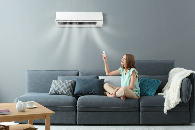 Aire acondicionado blanco en sala, mujer usando control remoto, ambiente moderno