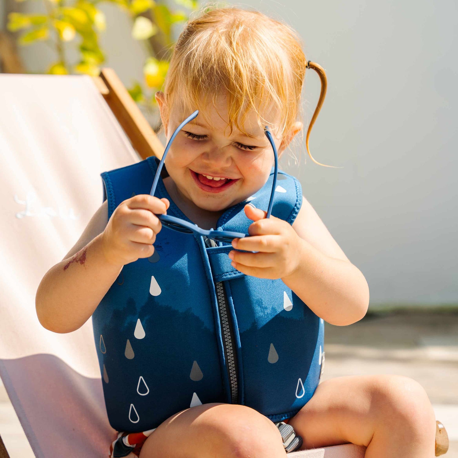 Chaleco azul para bebés, con diseño de gotas, usado por niña feliz al sol