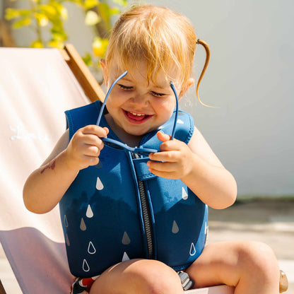 Chaleco azul para bebés, con diseño de gotas, usado por niña feliz al sol