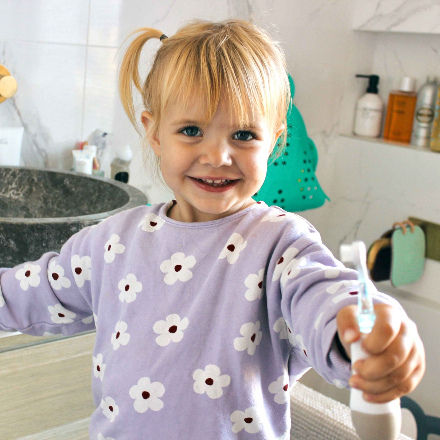 Niña sonriendo con cepillo en mano, baño moderno y decorado