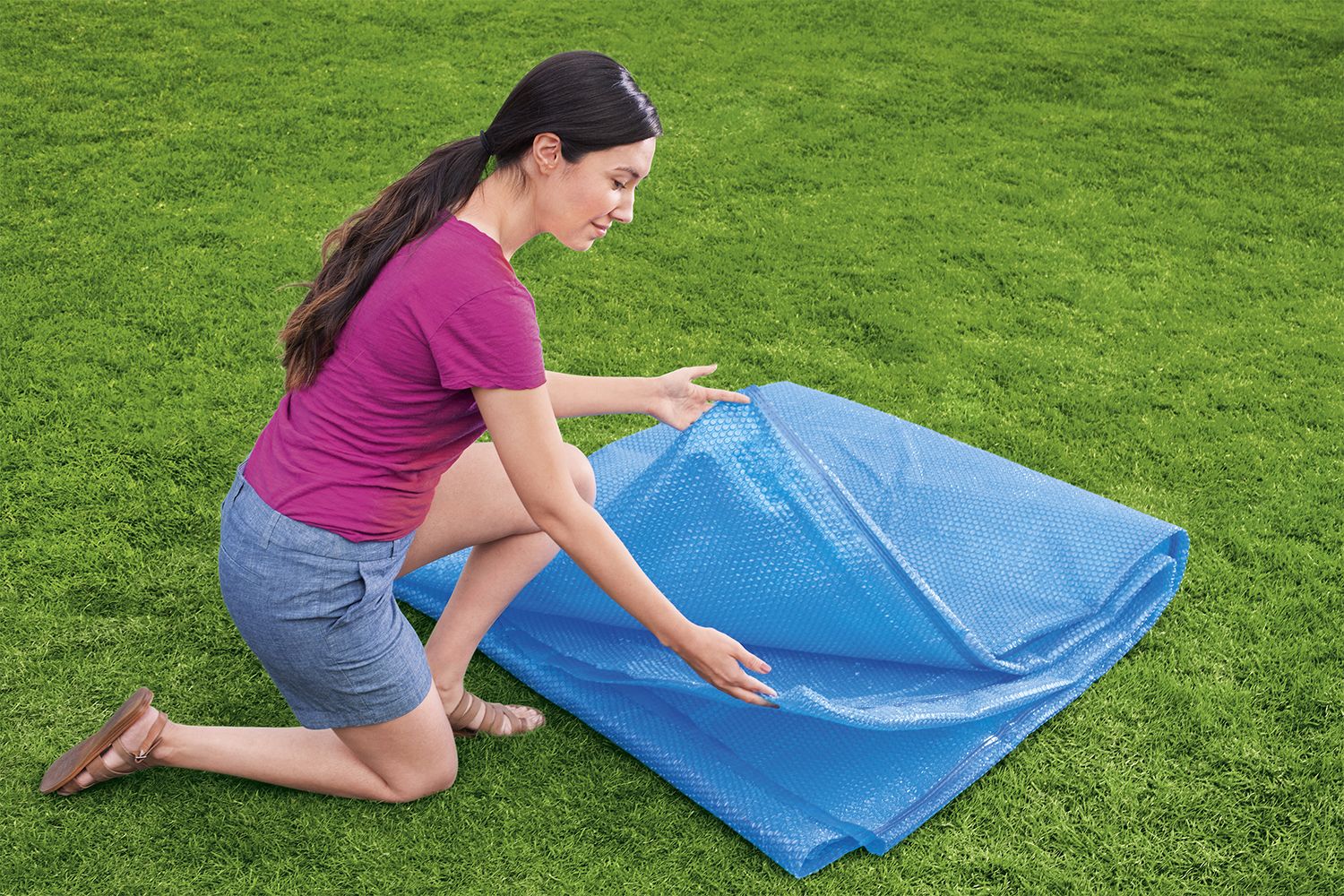 tapa protectora piscina desmontable azul, persona desplegando en el jardín