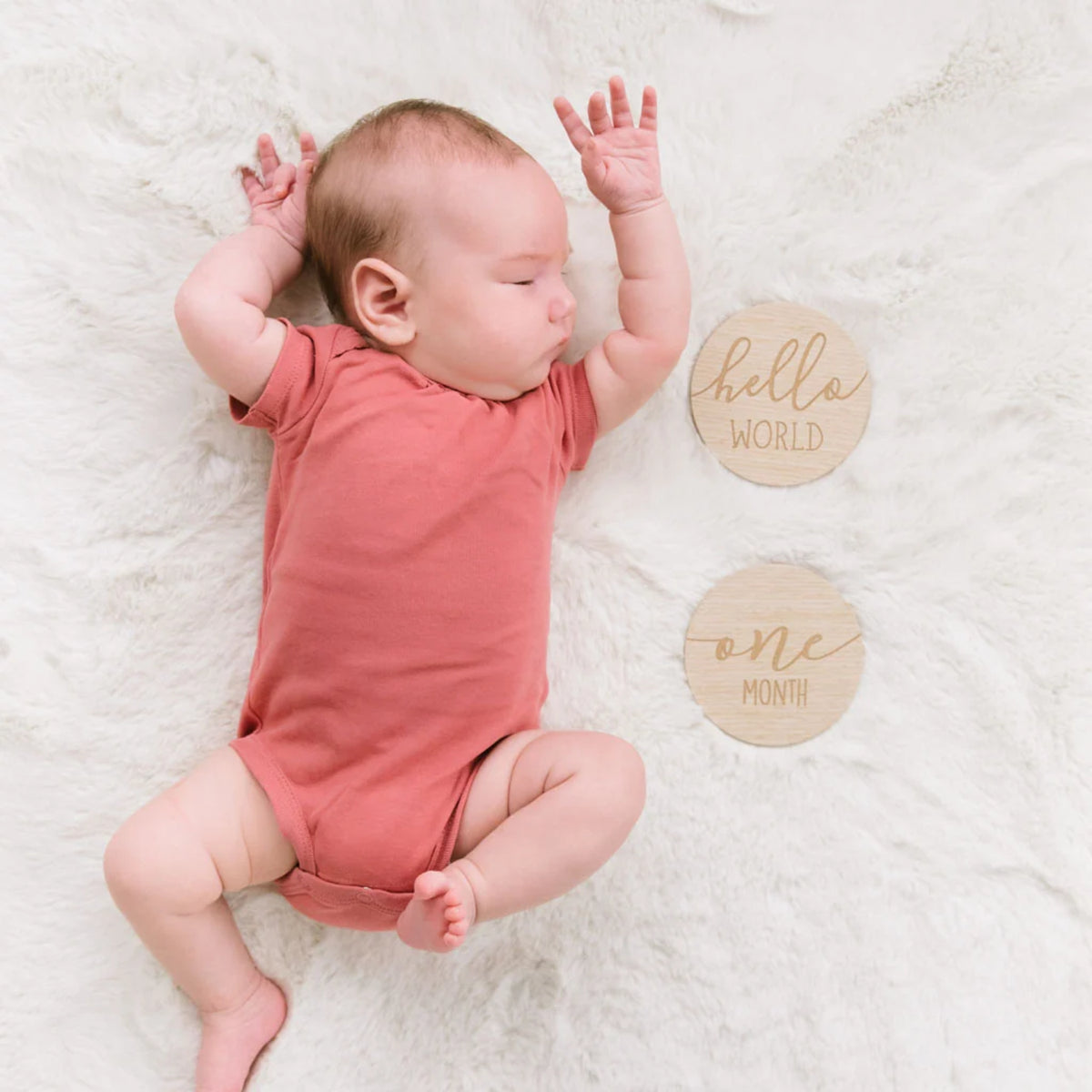 Bebé con body color terracota, bloques de madera 'hello world' y 'one month'