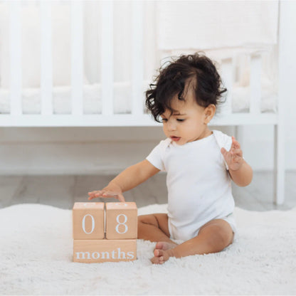 Bloques de madera con meses, bebé jugando en habitación blanca