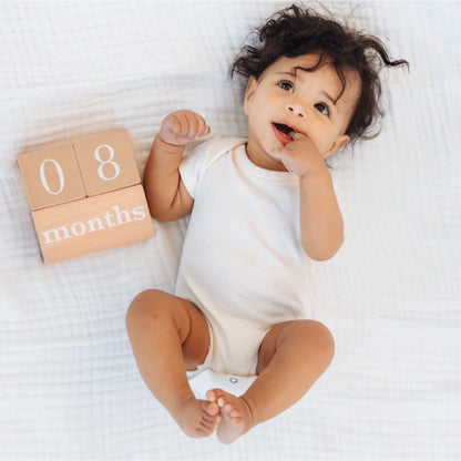 Bebé de ocho meses sonriente con bodysuit blanco y bloques de meses