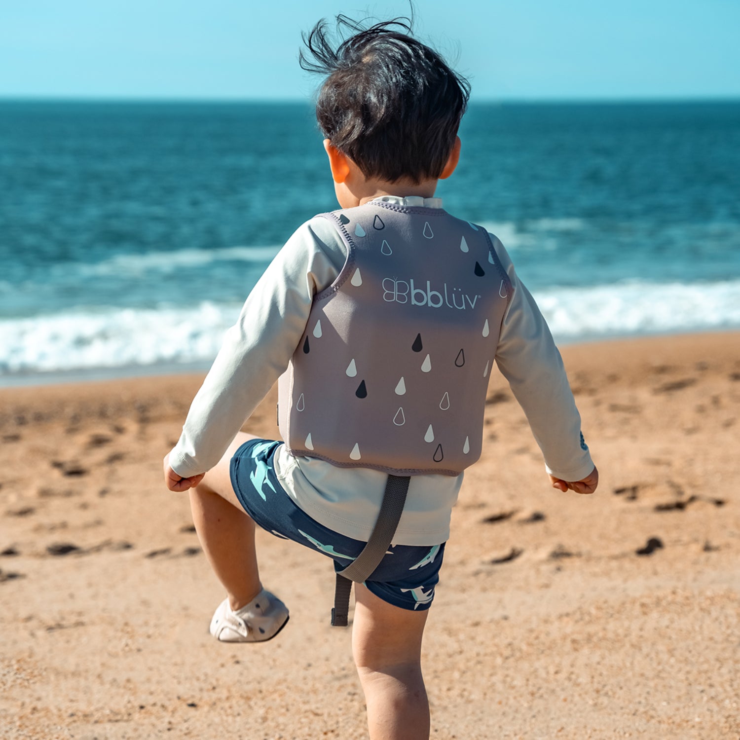 Chaleco BBLUV gris, niño jugando en la playa junto al mar