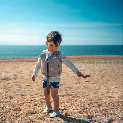 Chaleco BBLUV gris para niños en la playa con mar de fondo
