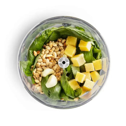 Licuadora transparente con espinacas, piñones y trozos de piña