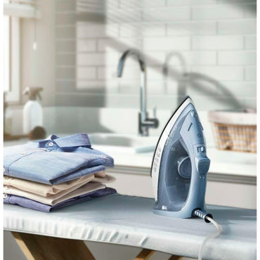 Plancha a vapor Frigidaire 1200W azul sobre mesa de planchar con camisas planchadas