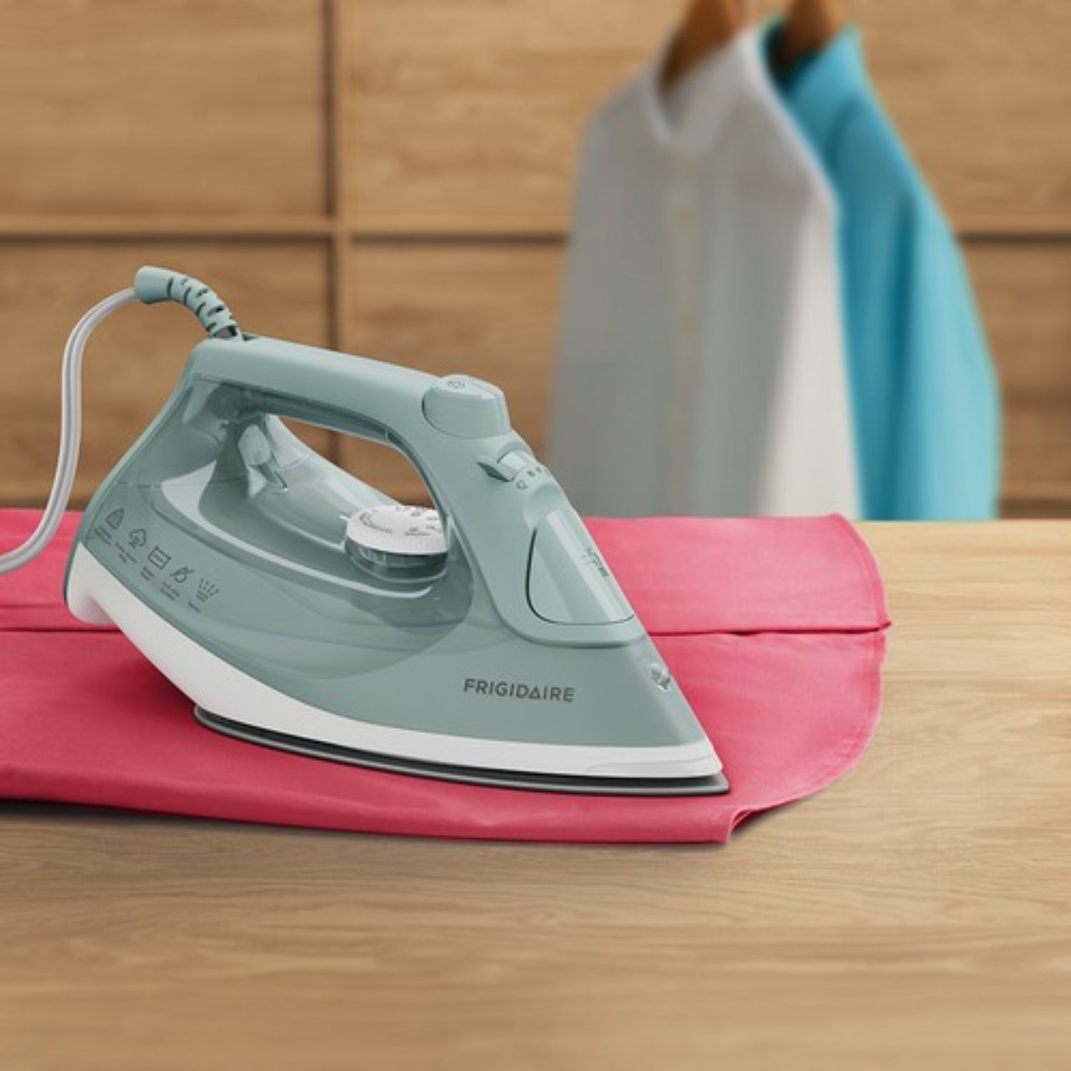 Plancha a vapor 1200W color verde, sobre tela rosa en mesa, vista frontal