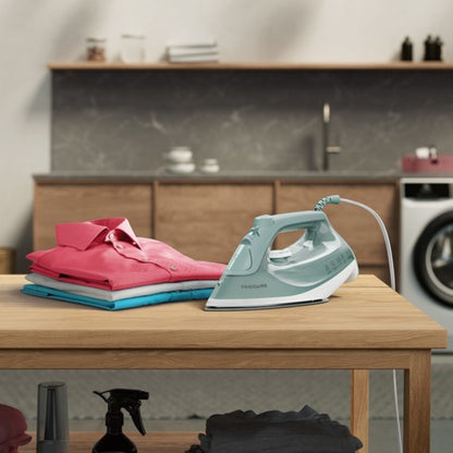 plancha a vapor 1200W en color verde sobre mesa con ropa planchada