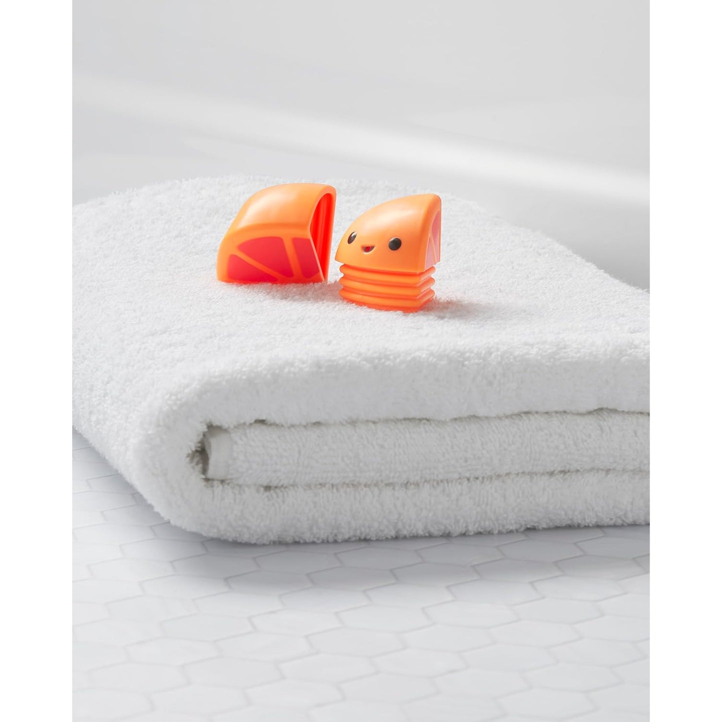 Juguete de baño naranja de SKIP*HOP en toalla blanca, para diversión en la hora del baño