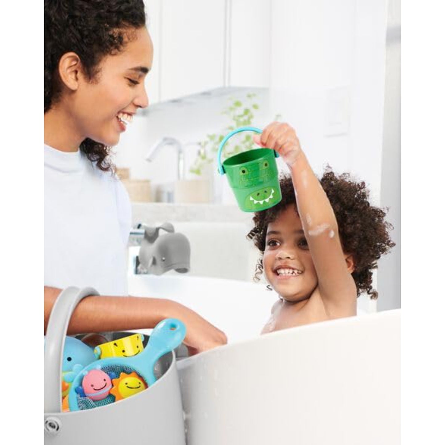 Juguetes de baño Skip Hop en una bañera, niño feliz sosteniendo balde verde
