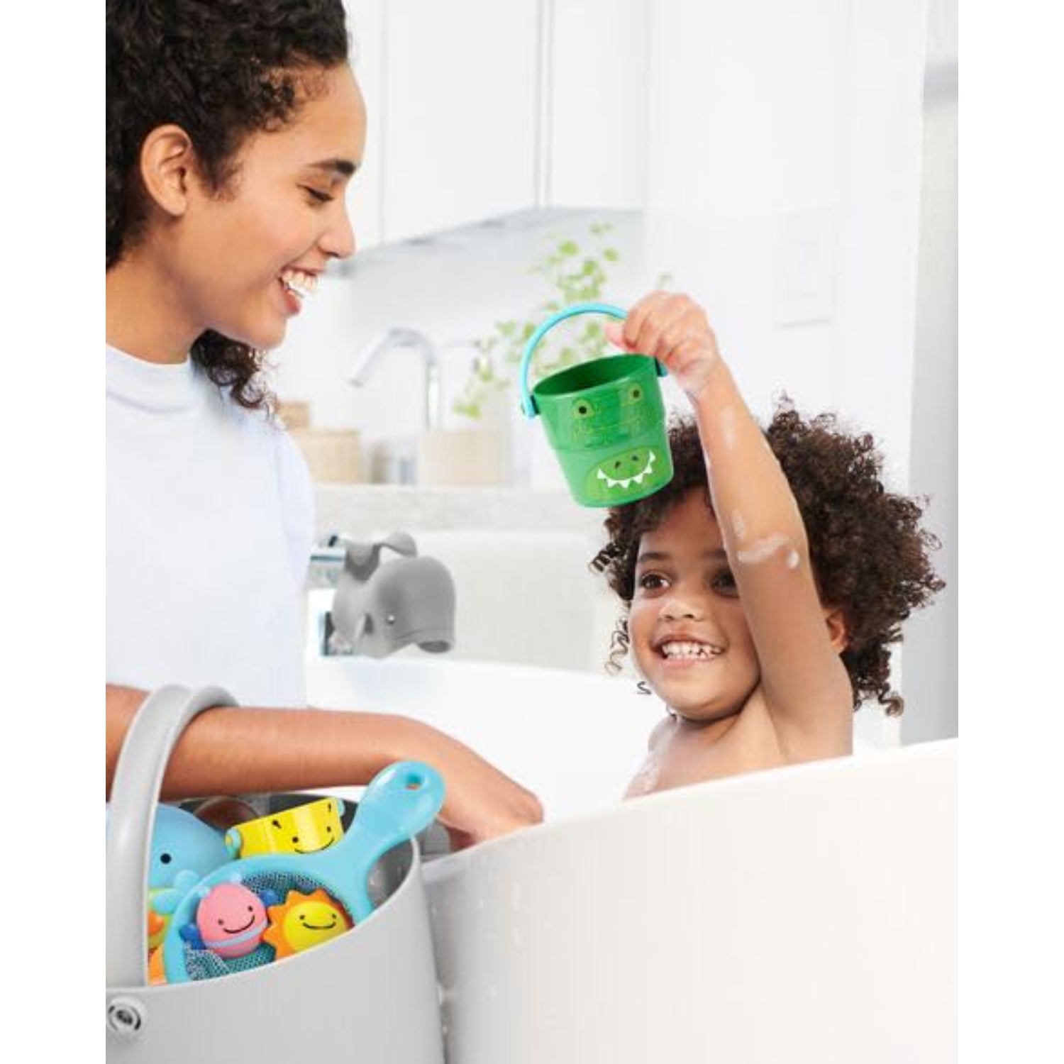 Juguetes de baño Skip Hop en una bañera, niño feliz sosteniendo balde verde