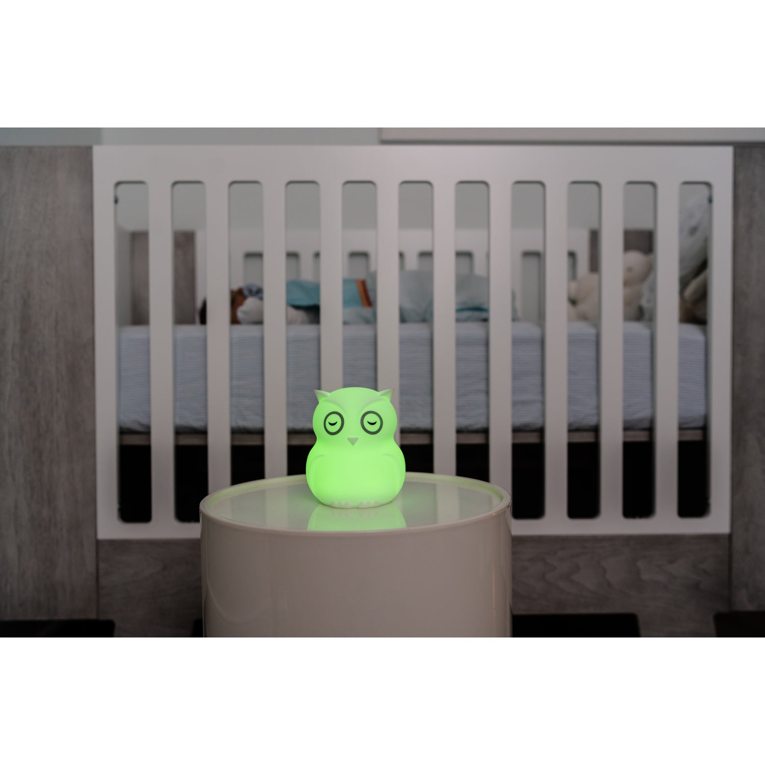 Lámpara búho verde en mesa junto a cuna en habitación infantil