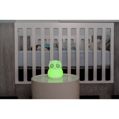 Lámpara búho verde en mesa junto a cuna en habitación infantil