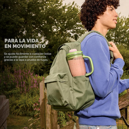 Licuadora verde en mochila, hombre caminando por sendero natural