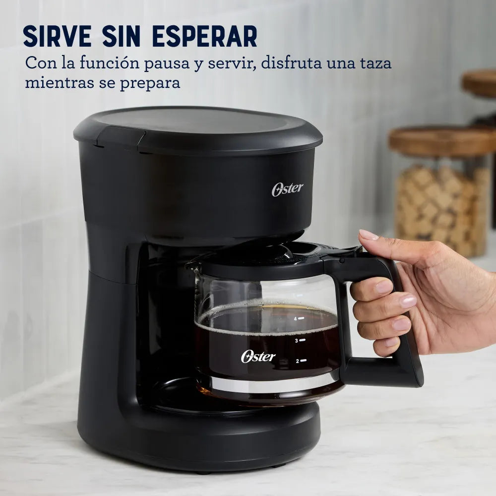 cafetera eléctrica Oster 5 tazas en negro con jarra de vidrio función pausa y servir y mano retirando jarra