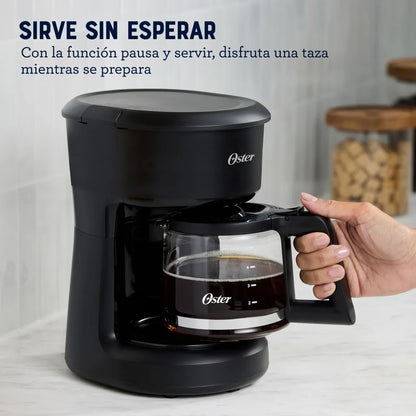 cafetera eléctrica Oster 5 tazas en negro con jarra de vidrio función pausa y servir y mano retirando jarra