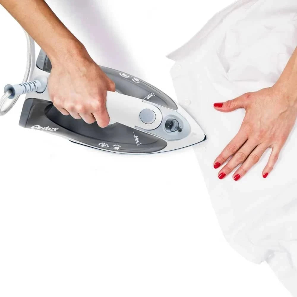 Plancha a vapor Oster para ropa en uso, alisando una camisa blanca con vapor efectivo