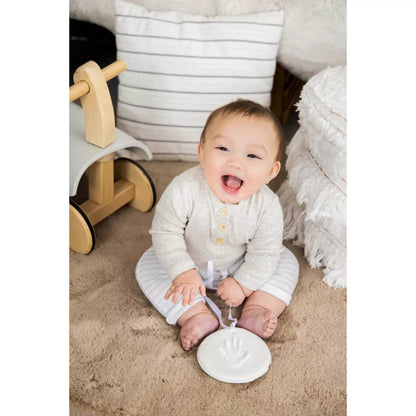 Bebé sonriendo en pijama gris, sentado en alfombra suave con decoración de hogar