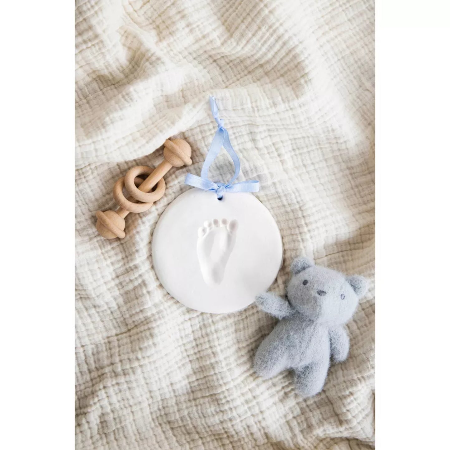 Placa de yeso con huella de pie de bebé, muñequito gris y sonajero de madera