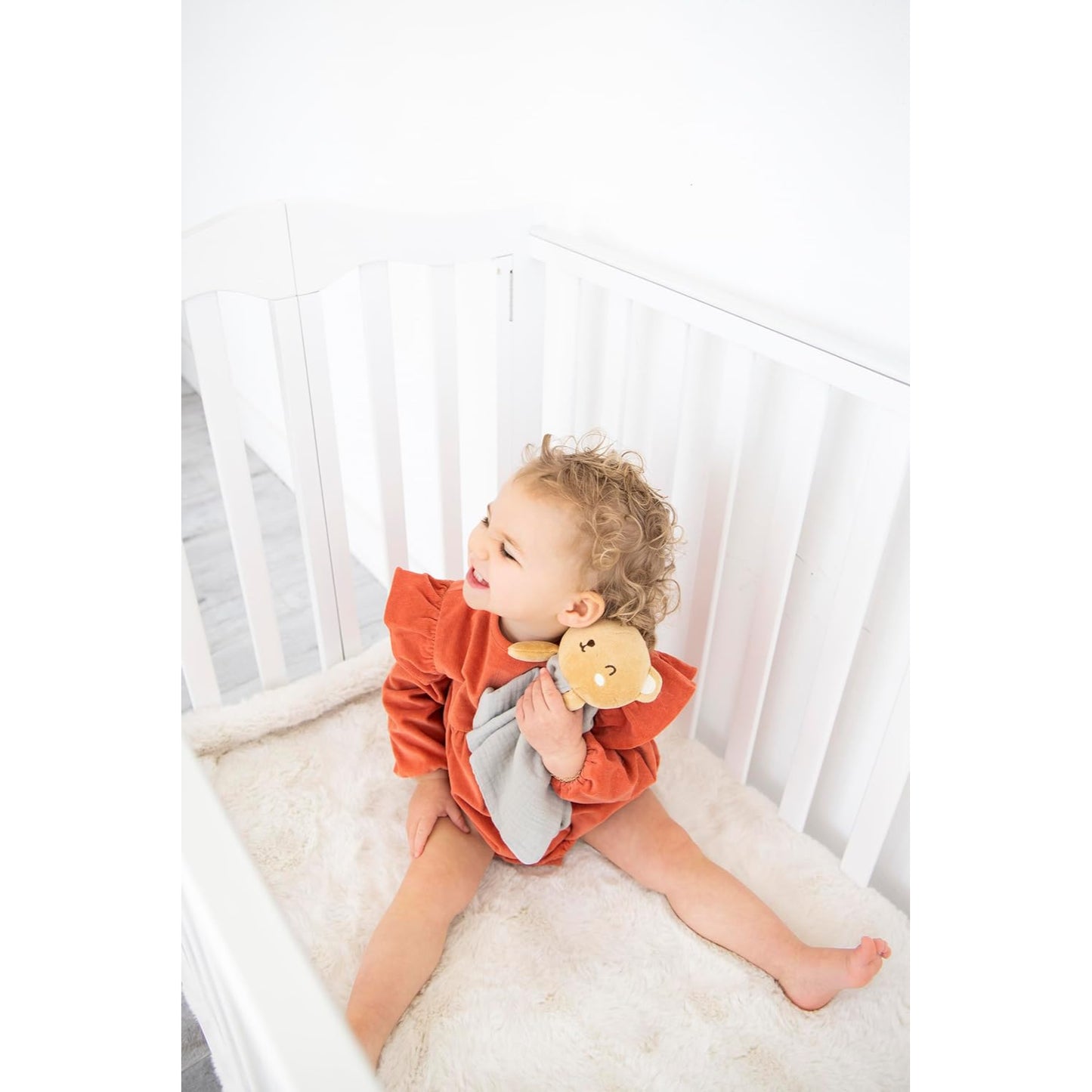 Niño feliz en cuna con juguete de león, ropa naranja y gris.