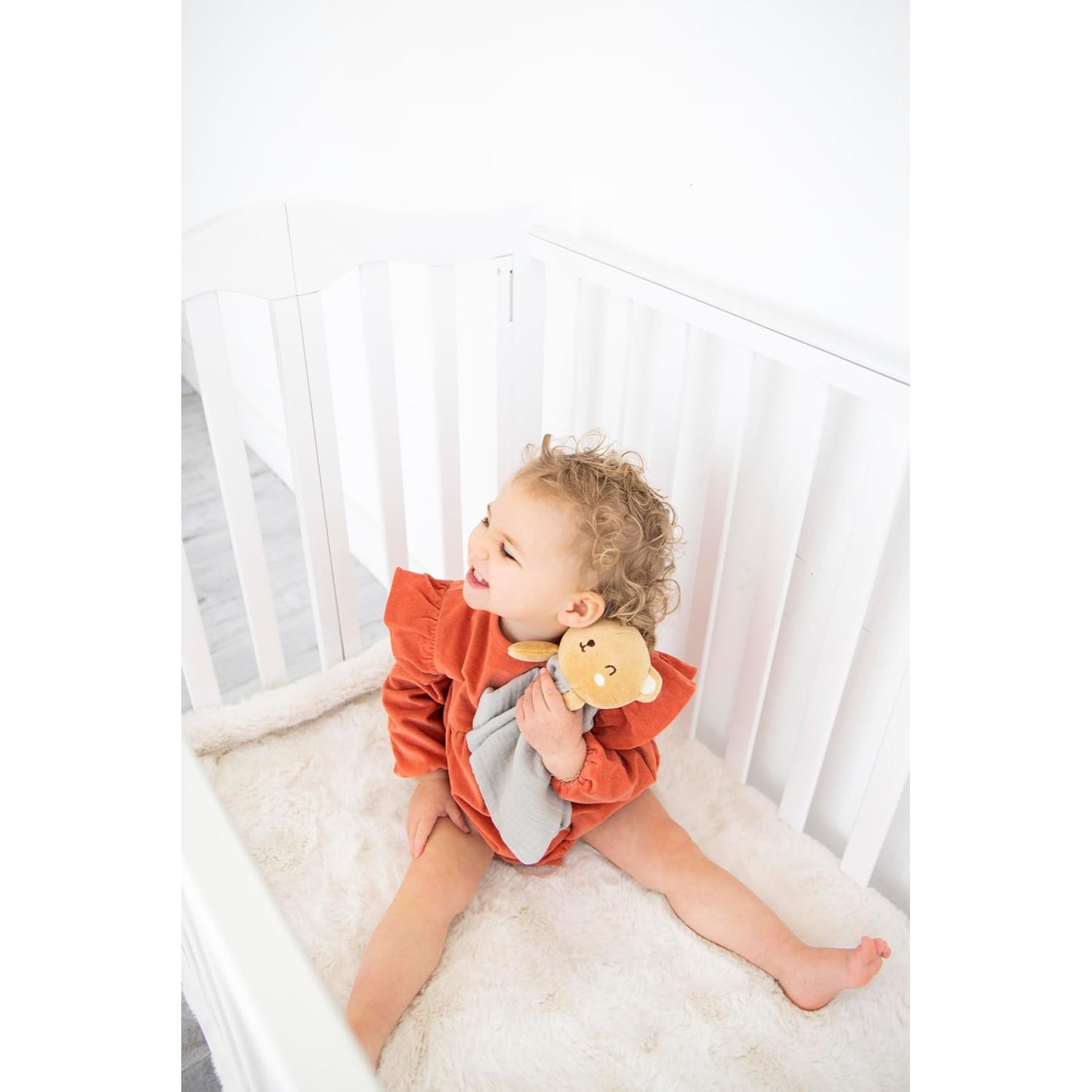 Niño feliz en cuna con juguete de león, ropa naranja y gris.