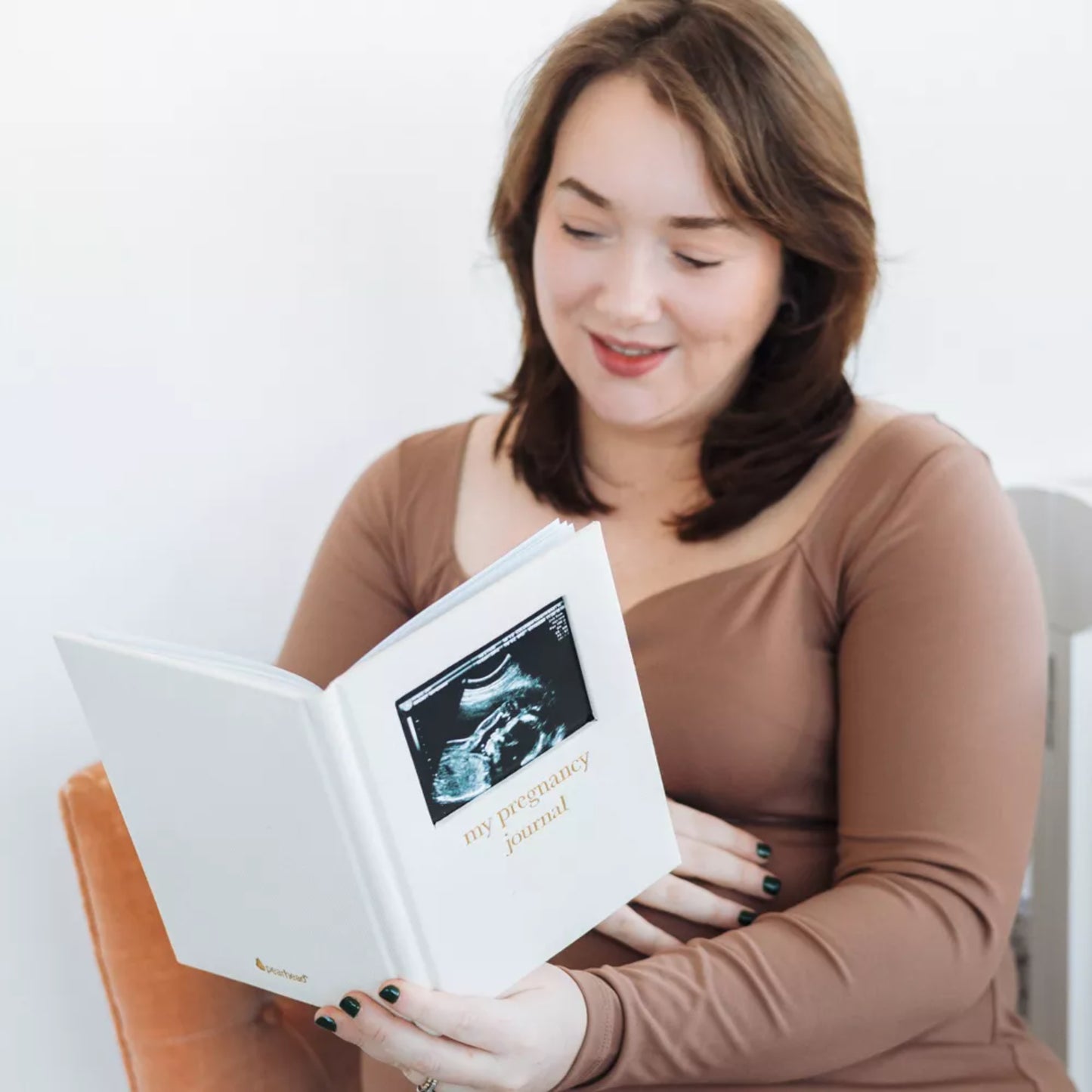 Diario de embarazo blanco con foto de ultrasonido, mujer leyendo en casa