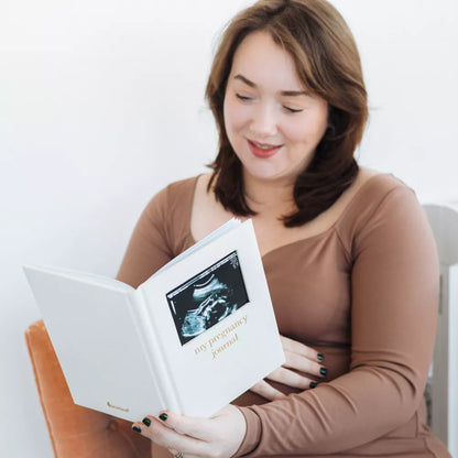 Diario de embarazo blanco con foto de ultrasonido, mujer leyendo en casa