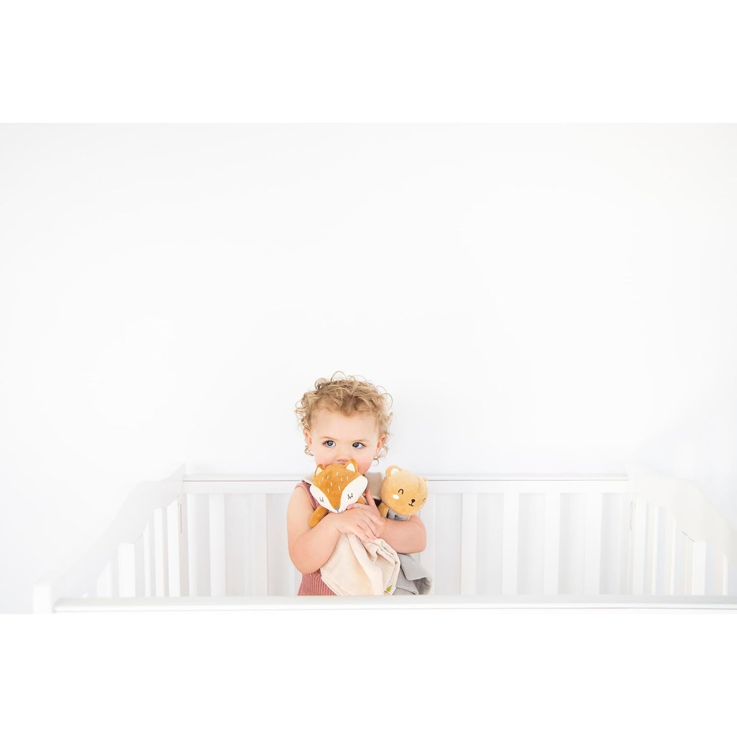 Niña con muñecos de peluche en cuna blanca, juego y ternura