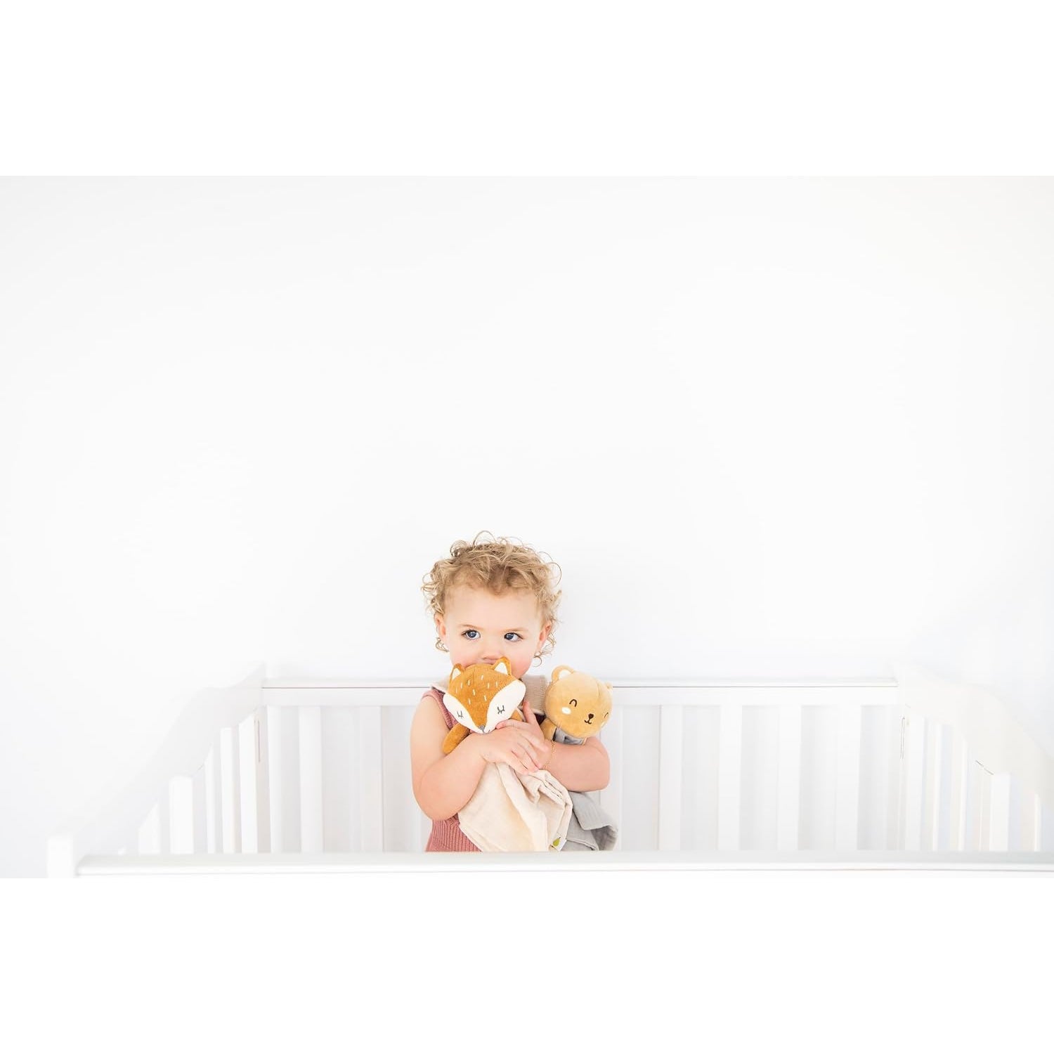 Niña con muñecos de peluche en cuna blanca, juego y ternura