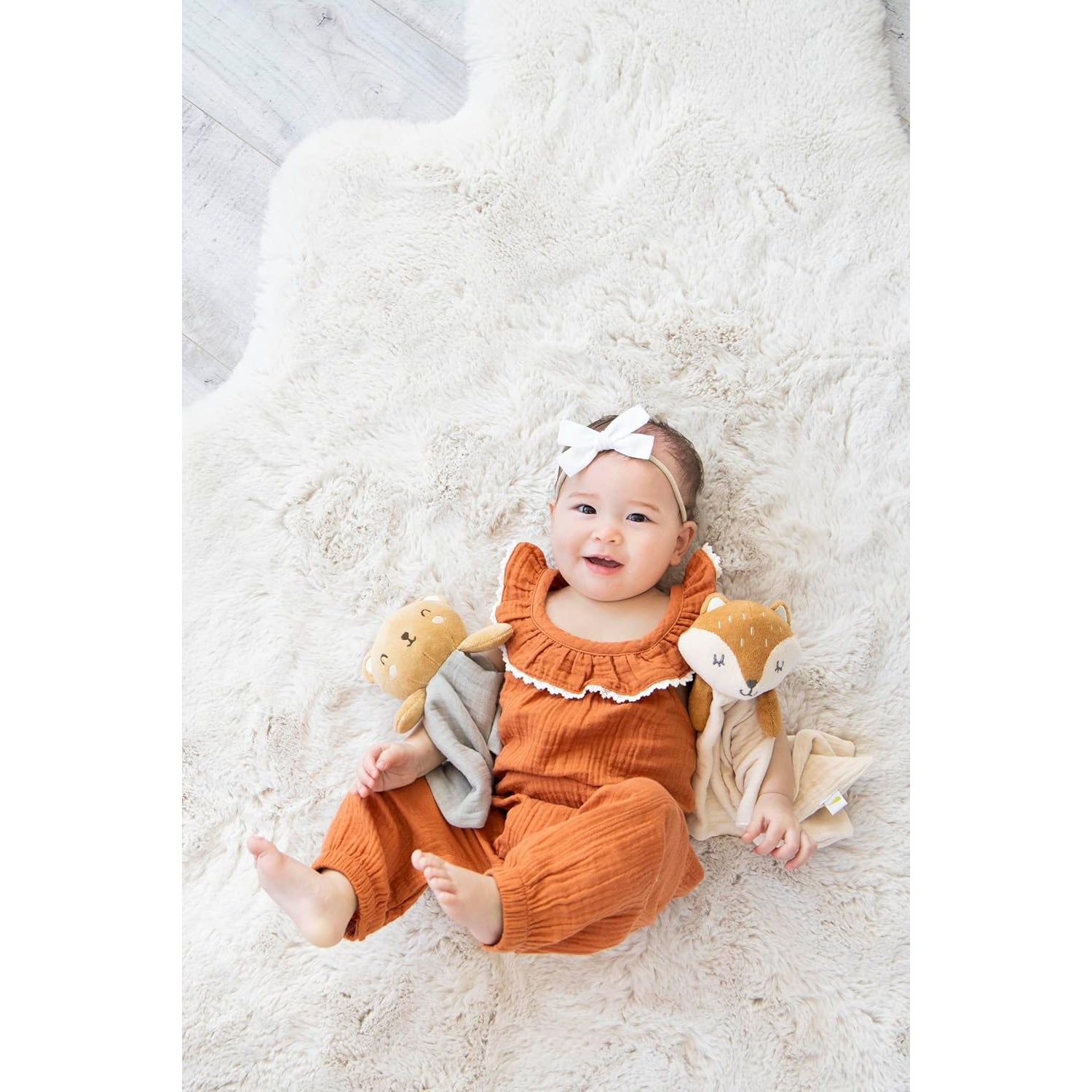 Niña bebé con overol naranja sosteniendo peluches en alfombra suave