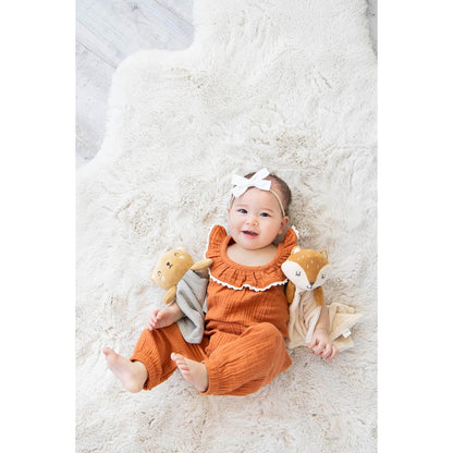 Niña bebé con overol naranja sosteniendo peluches en alfombra suave