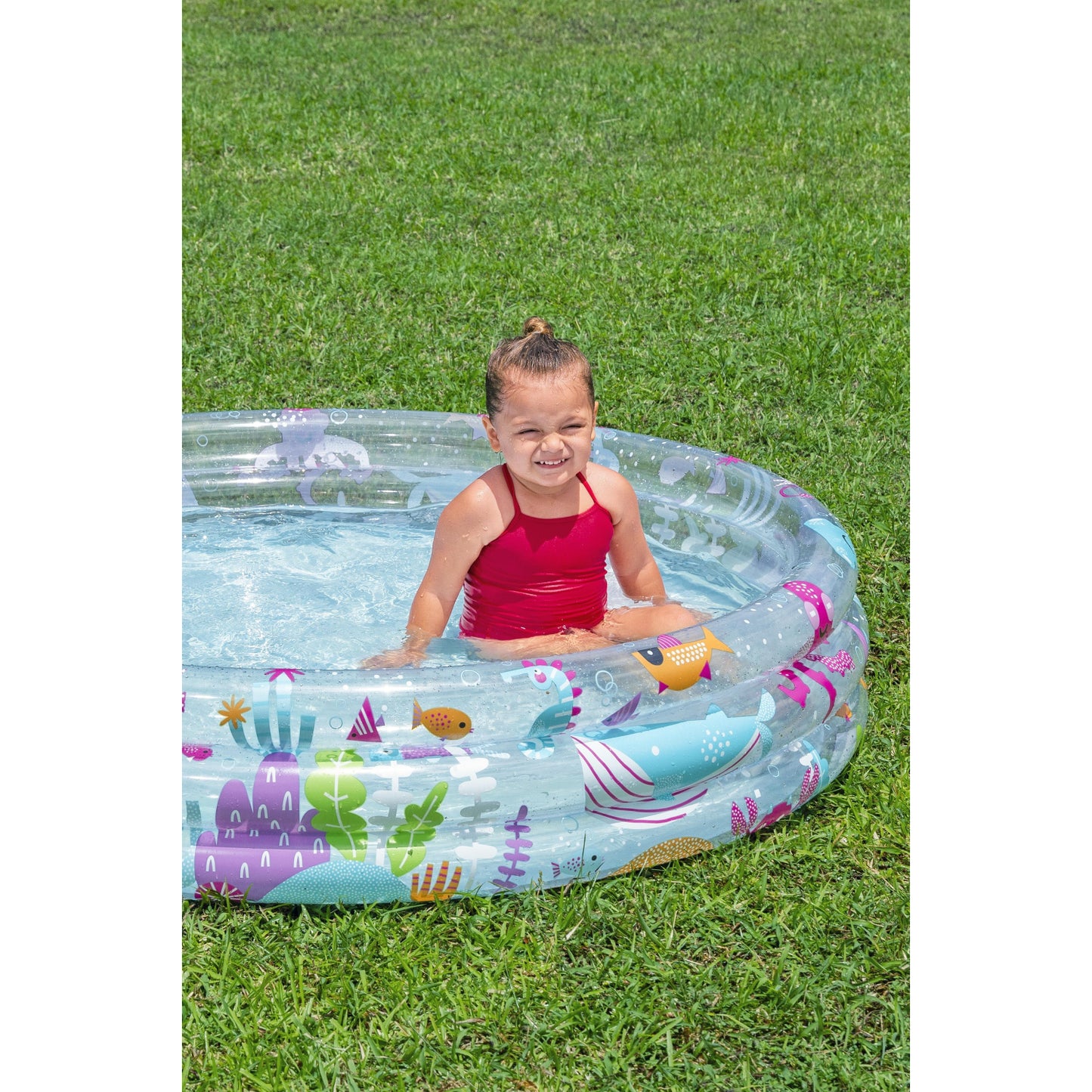 Piscina hinchable infantil transparente con dibujos coloridos y niña contenta dentro