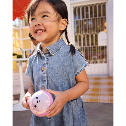 Niña con vestido de mezclilla sujetando snack rosa de Skip Hop