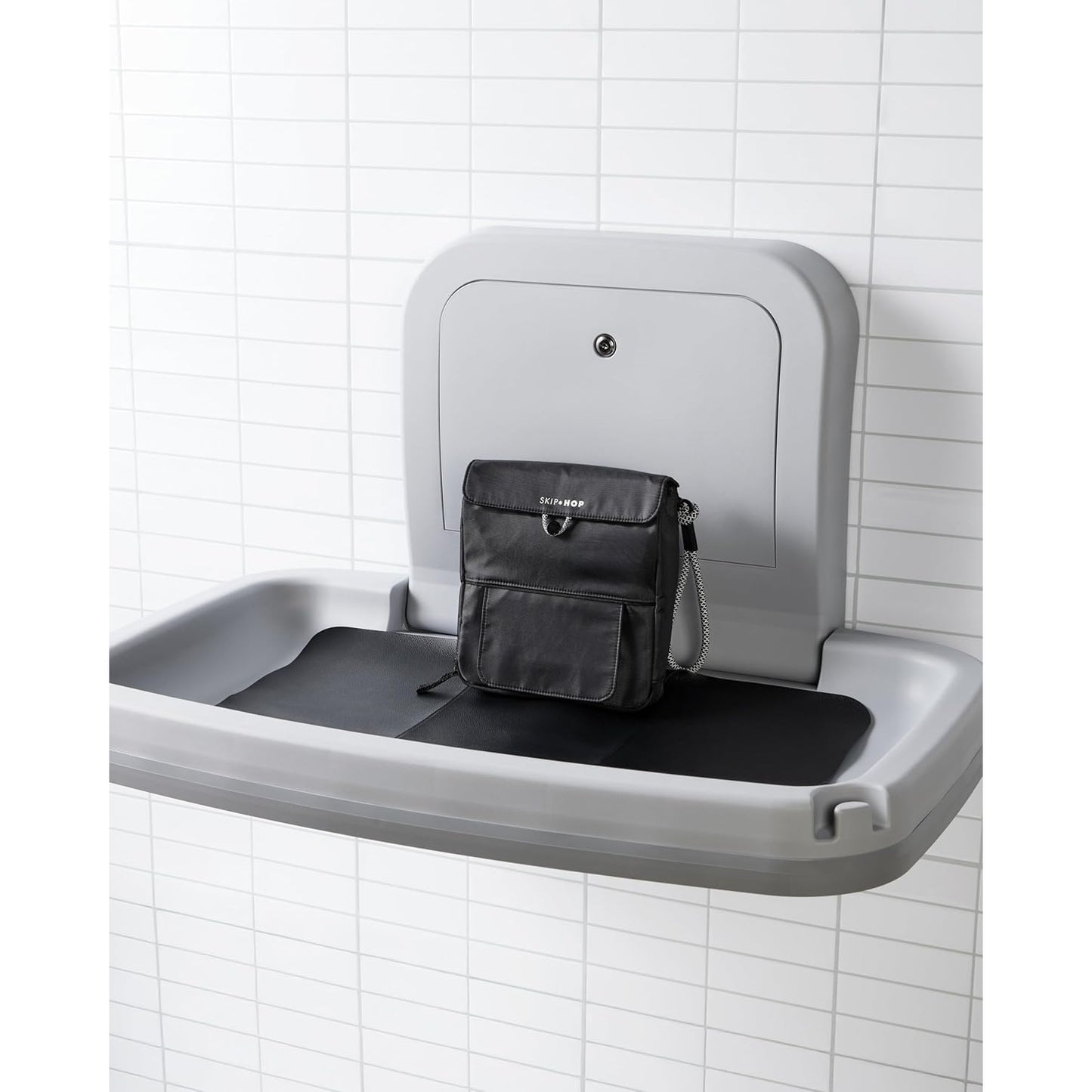 Cambiador gris montado en la pared con bolsa negra, ideal para baños infantiles