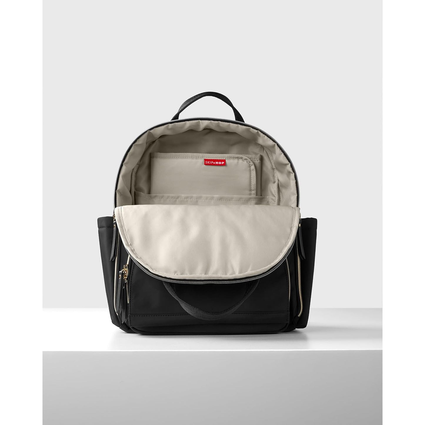 Mochila negra SKIP*HOP vista frontal con interior claro y compartimentos organizadores