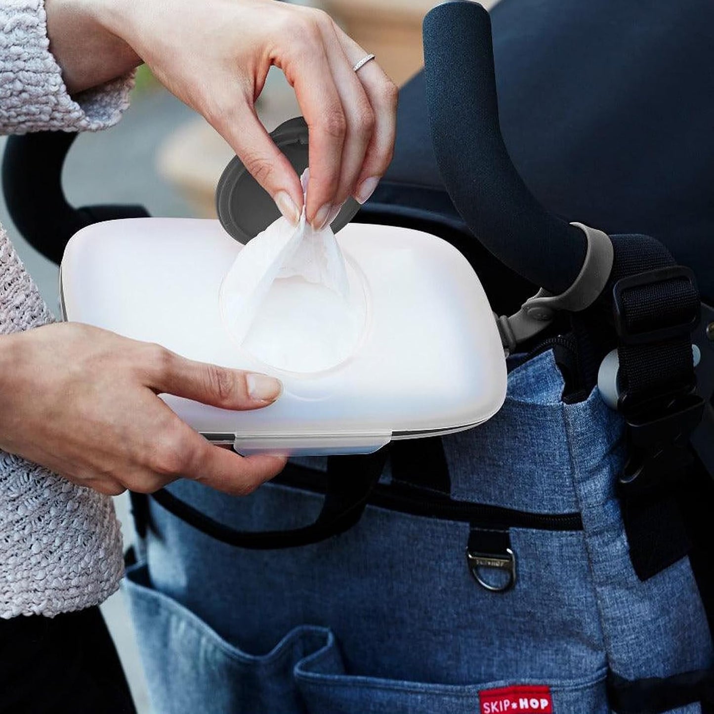 Contenedor blanco para toallitas SKIP*HOP, vista desde mano con carrito de bebé