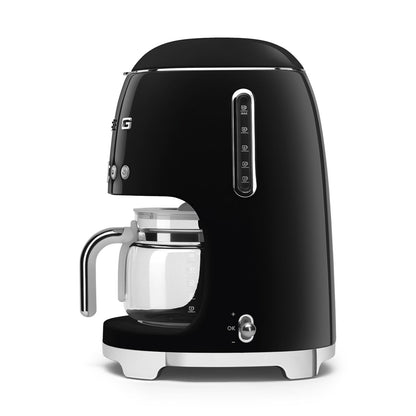 Cafetera negra SMEG vista lateral con jarra de vidrio y botón de control