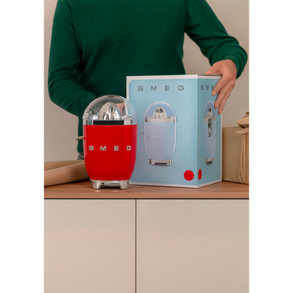 Exprimidor rojo SMEG en mesa junto a su caja, vista frontal