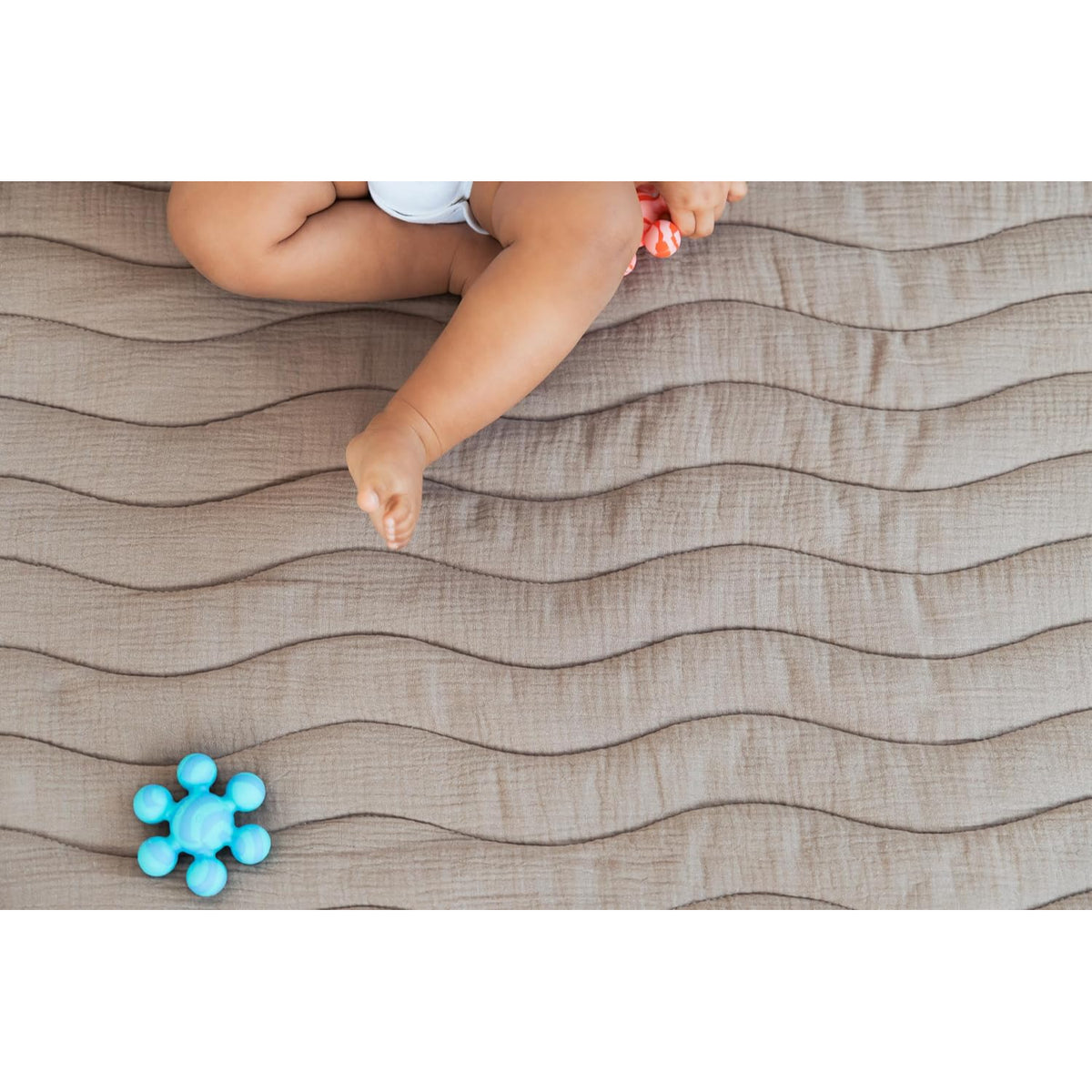 Manta para bebés en color beige con textura ondulada y juguete azul