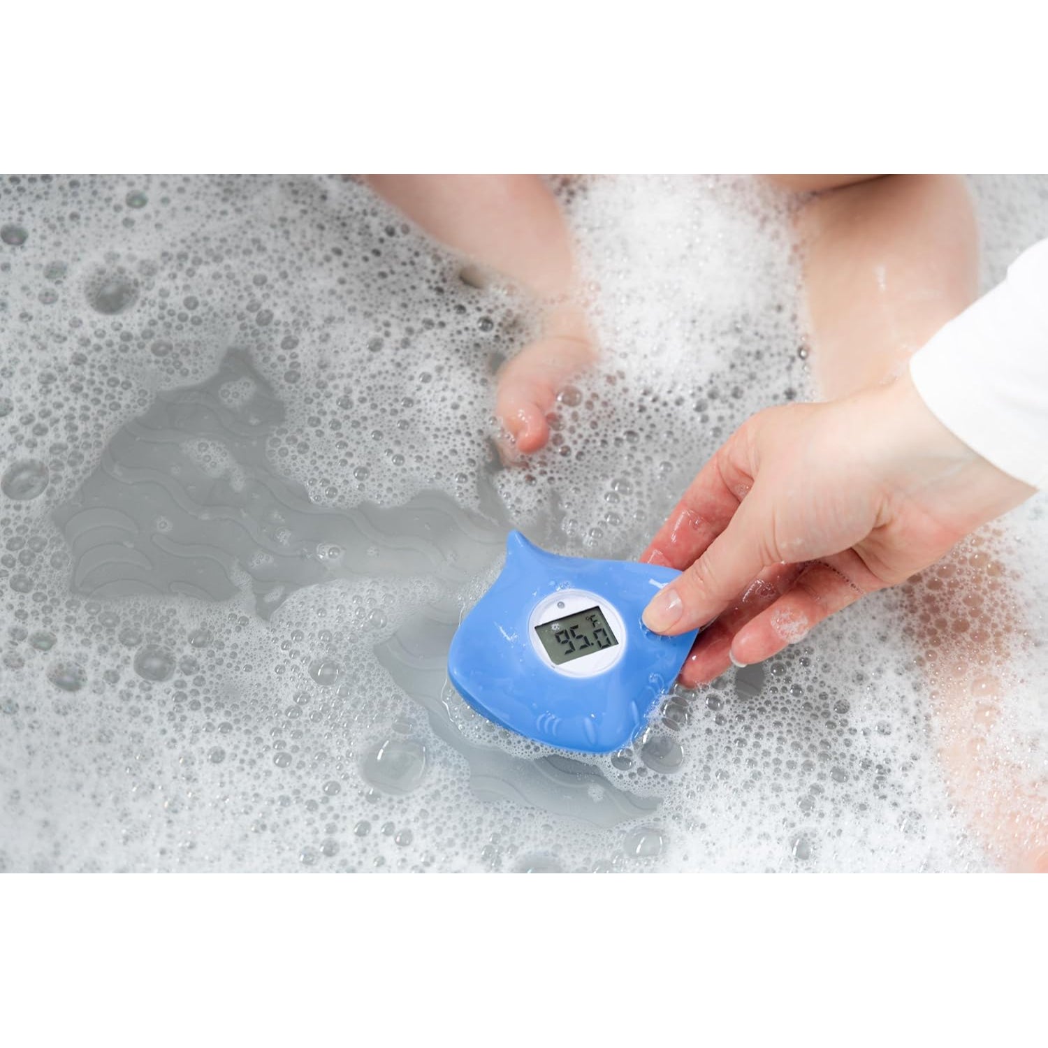 Termómetro de baño azul, mano sosteniéndolo, agua espumosa y pies de bebé